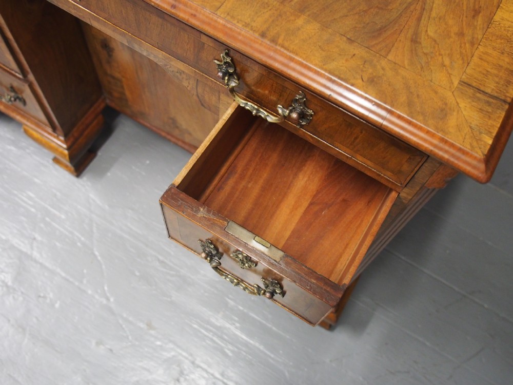 A George II style walnut kneehole desk featuring figured wood veneers, a central cupboard in the recessed kneehole, multi-drawer storage with brass backplate handles, and bracket feet. View IV