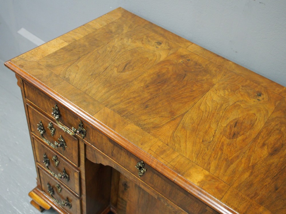 A George II style walnut kneehole desk featuring figured wood veneers, a central cupboard in the recessed kneehole, multi-drawer storage with brass backplate handles, and bracket feet. View XI
