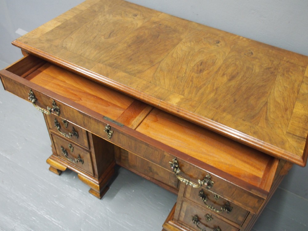 A George II style walnut kneehole desk featuring figured wood veneers, a central cupboard in the recessed kneehole, multi-drawer storage with brass backplate handles, and bracket feet. View XIII