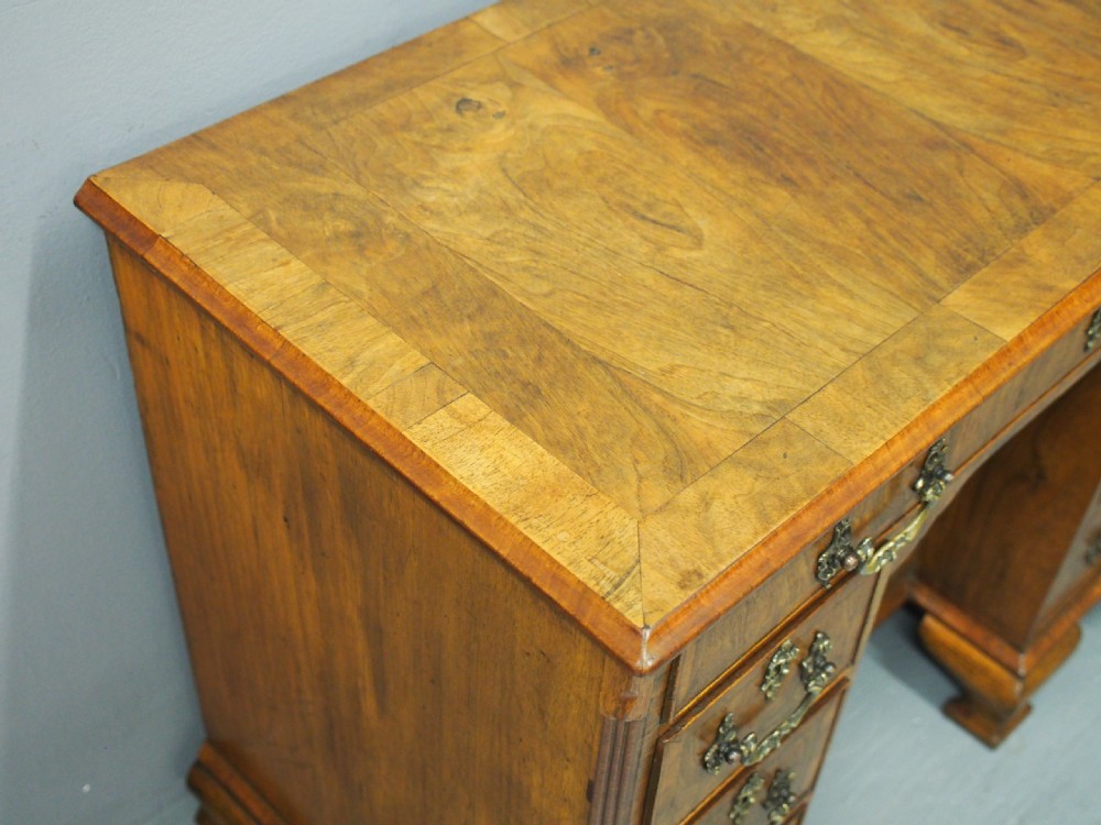 A George II style walnut kneehole desk featuring figured wood veneers, a central cupboard in the recessed kneehole, multi-drawer storage with brass backplate handles, and bracket feet. View XIV