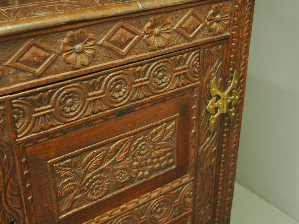 A dark carved oak Charles II court cupboard featuring intricate floral relief panels, turned supports, inscribed initials, and decorative brass hinges. View IX