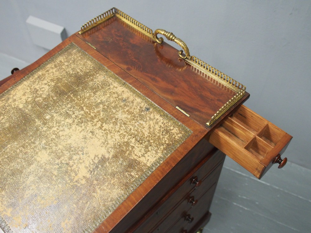 A George IV mahogany Davenport desk with a sloped gold-tooled leather top, upper brass gallery, open side shelving, and brass castors. View X
