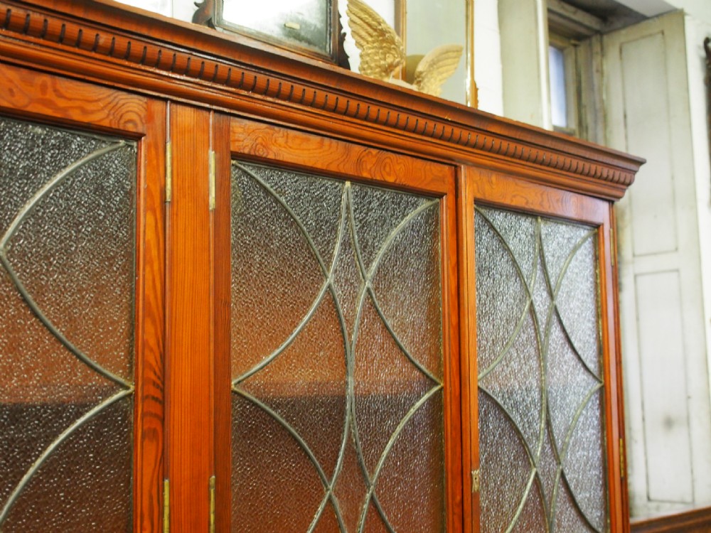 A large Victorian pitch pine bookcase cabinet featuring four upper glazed doors with geometric leaded glass and four lower panelled cupboard doors. View II