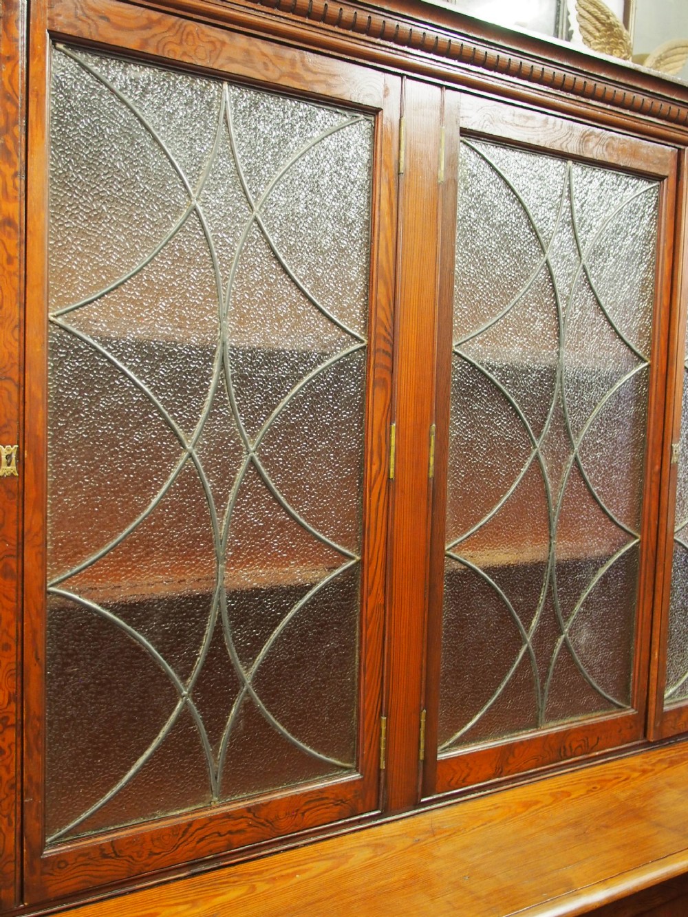 A large Victorian pitch pine bookcase cabinet featuring four upper glazed doors with geometric leaded glass and four lower panelled cupboard doors. View IV