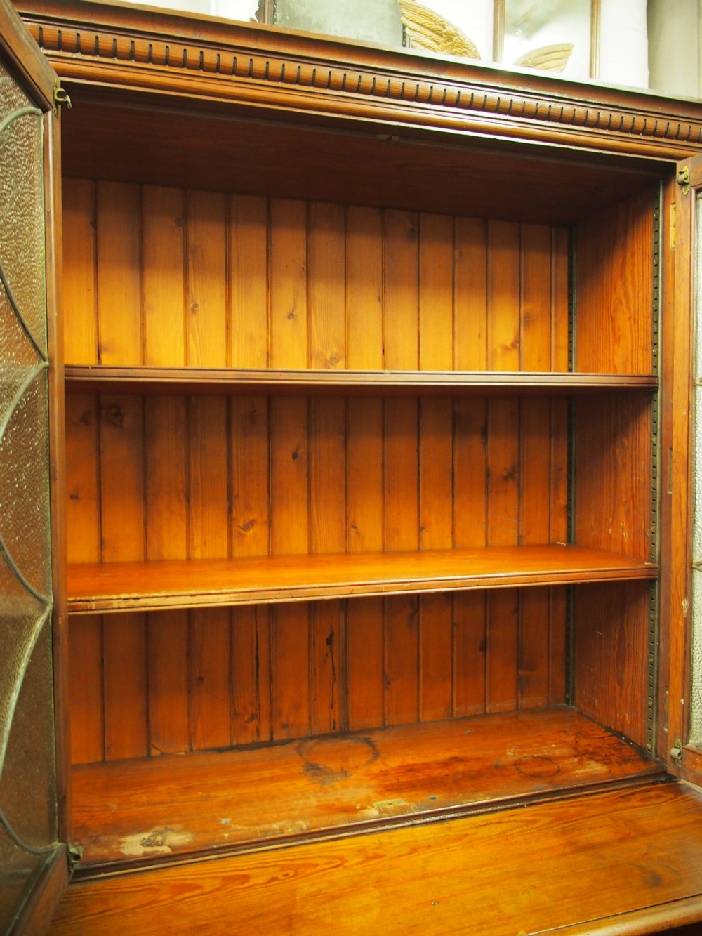 A large Victorian pitch pine bookcase cabinet featuring four upper glazed doors with geometric leaded glass and four lower panelled cupboard doors. View V