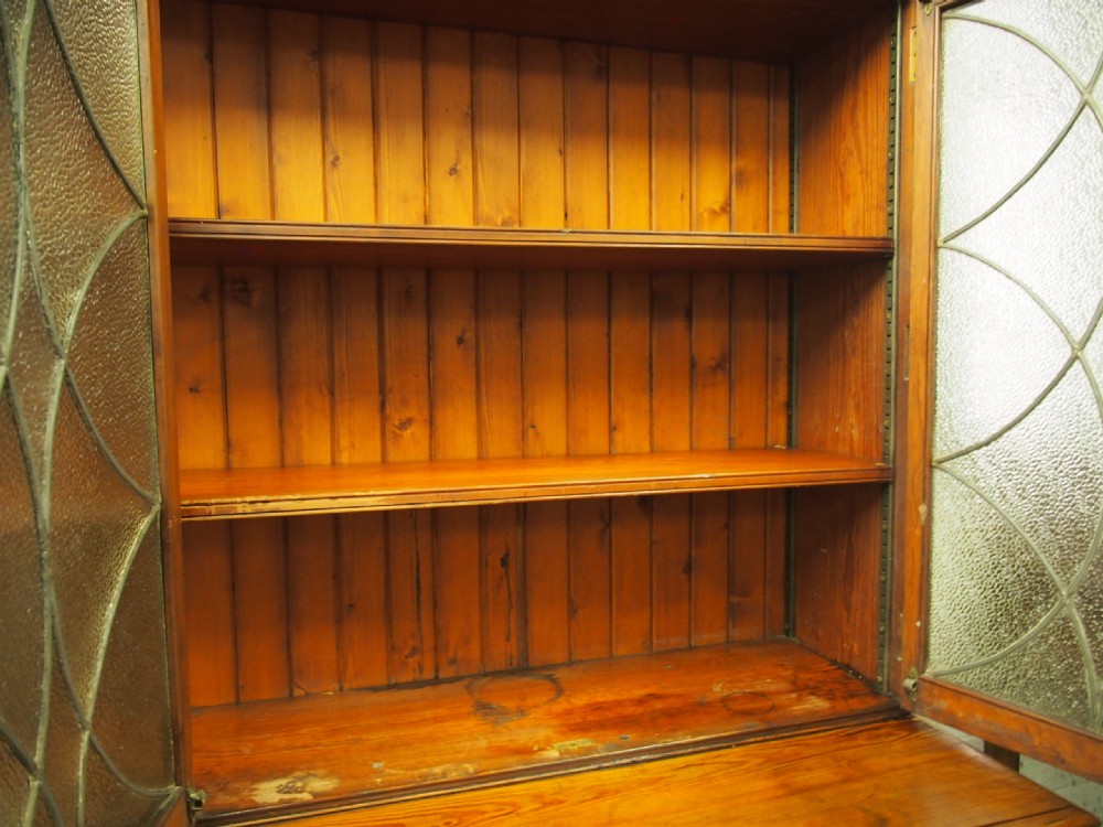 A large Victorian pitch pine bookcase cabinet featuring four upper glazed doors with geometric leaded glass and four lower panelled cupboard doors. View VI