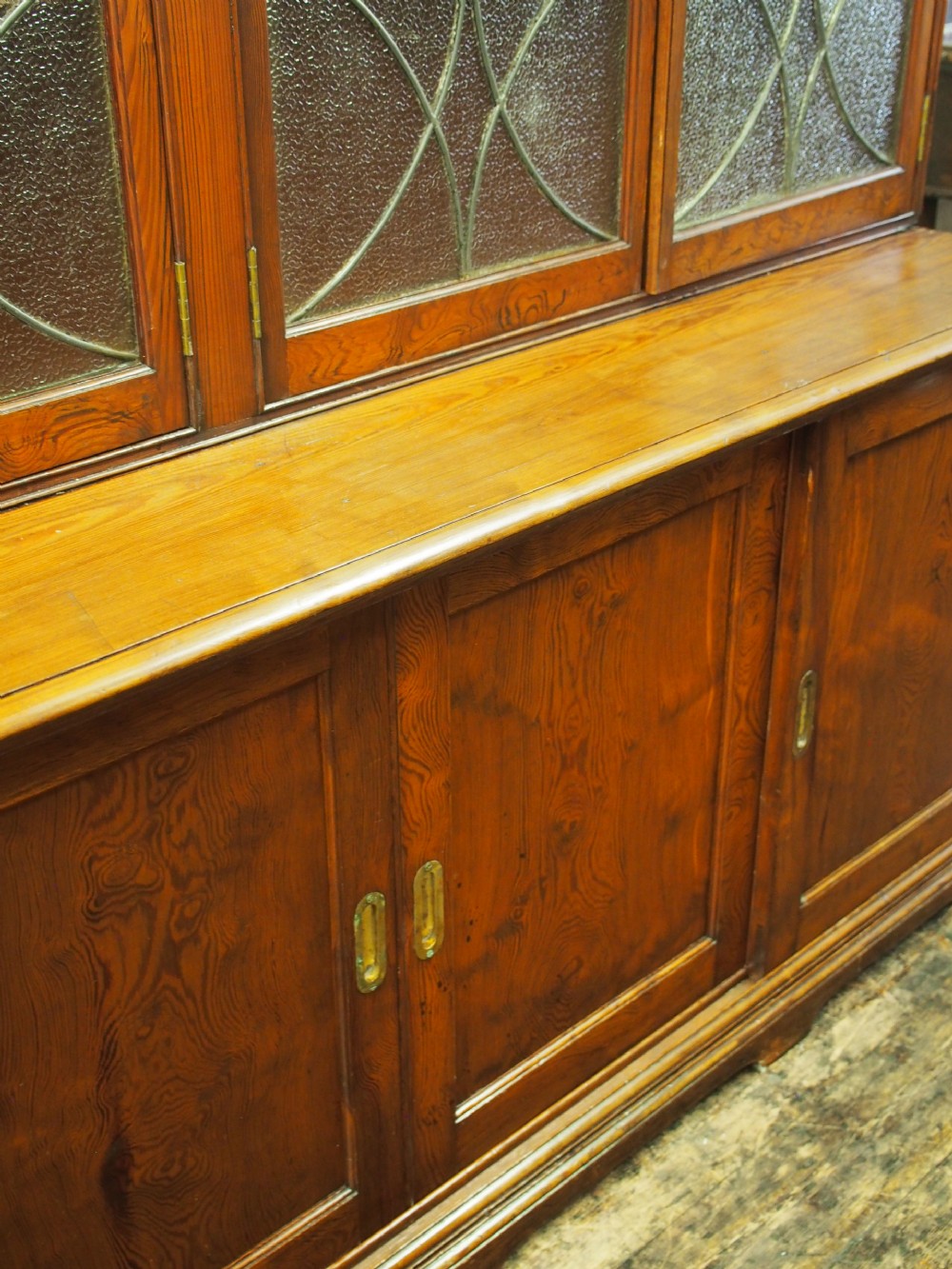 A large Victorian pitch pine bookcase cabinet featuring four upper glazed doors with geometric leaded glass and four lower panelled cupboard doors. View VIII
