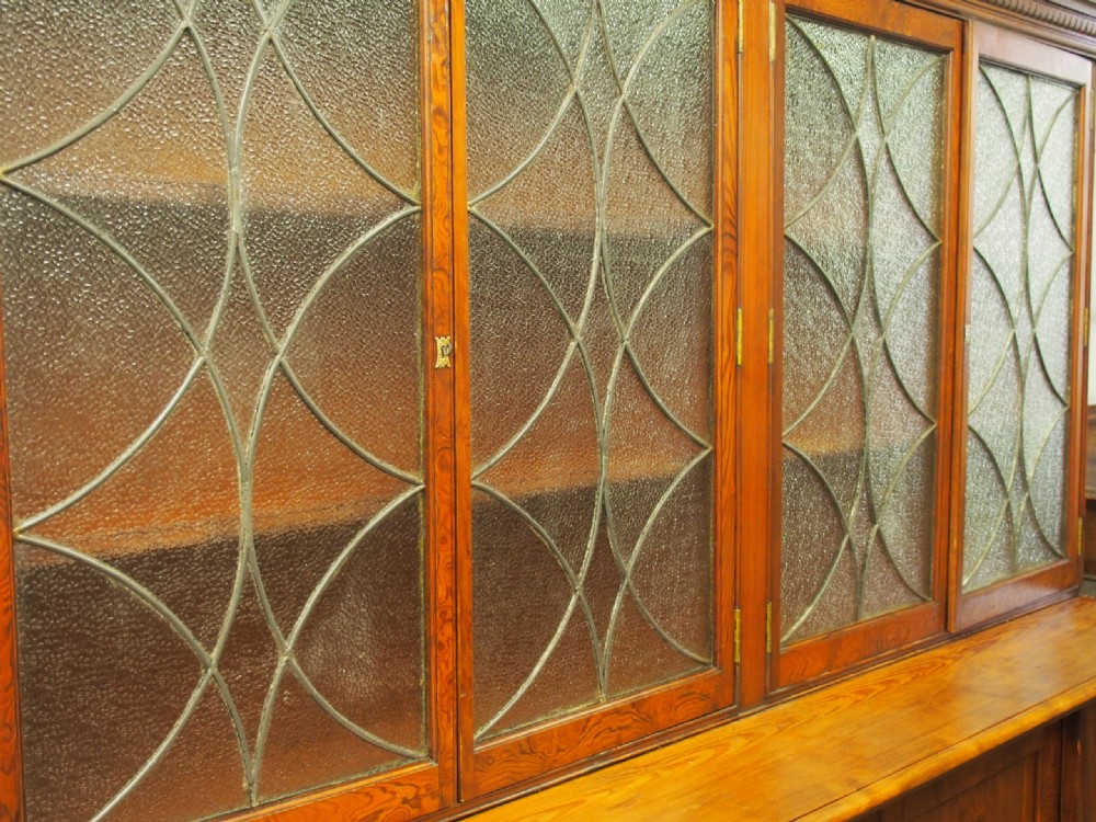 A large Victorian pitch pine bookcase cabinet featuring four upper glazed doors with geometric leaded glass and four lower panelled cupboard doors. View IX