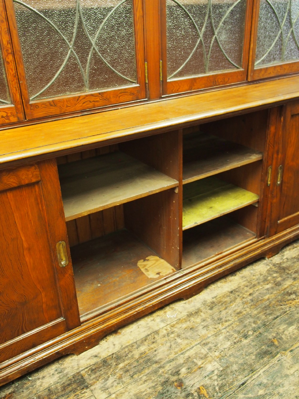 A large Victorian pitch pine bookcase cabinet featuring four upper glazed doors with geometric leaded glass and four lower panelled cupboard doors. View X
