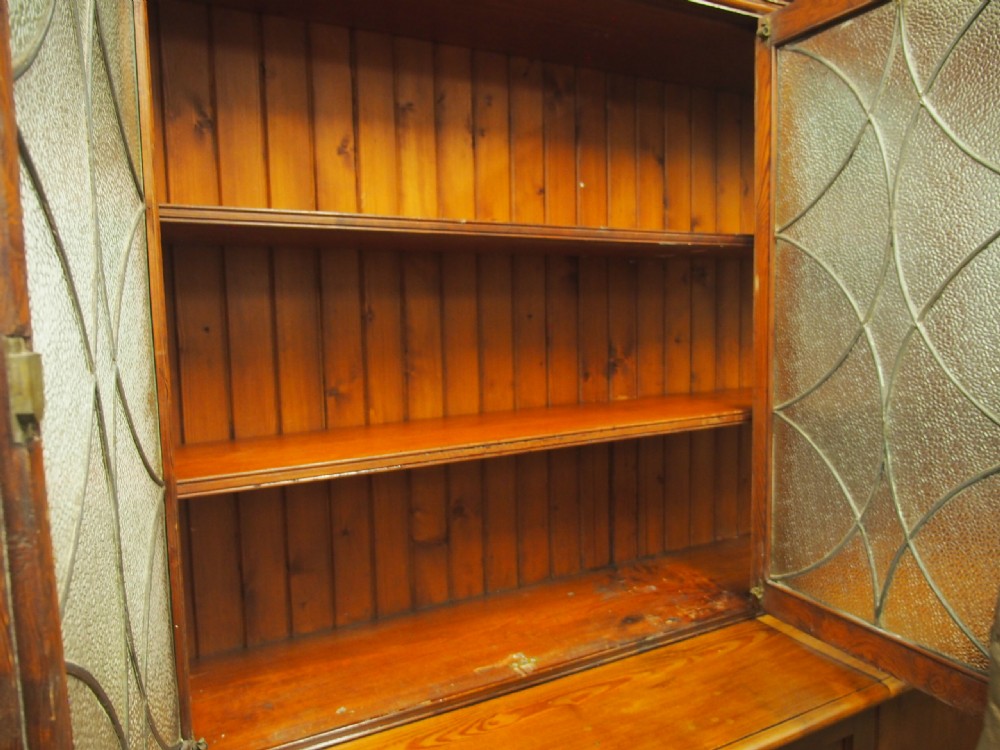 A large Victorian pitch pine bookcase cabinet featuring four upper glazed doors with geometric leaded glass and four lower panelled cupboard doors. View XI