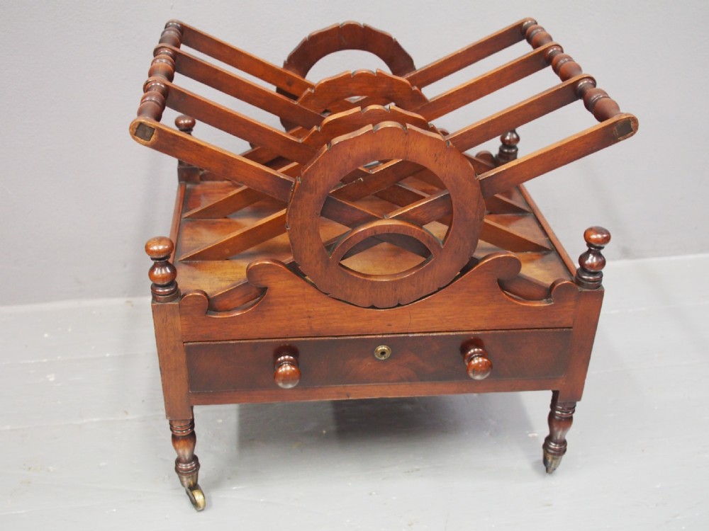 A George IV mahogany Canterbury featuring carved circular dividers, turned corner posts, a single base drawer with two wooden turned knobs, and legs set on brass castors. View III