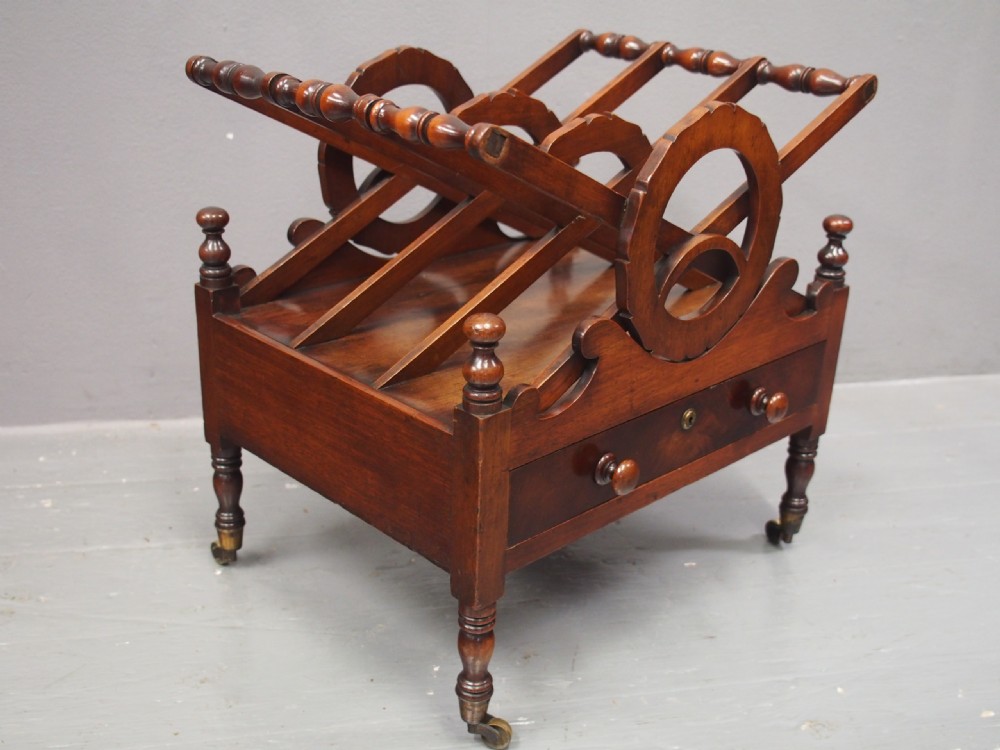 A George IV mahogany Canterbury featuring carved circular dividers, turned corner posts, a single base drawer with two wooden turned knobs, and legs set on brass castors. View IV