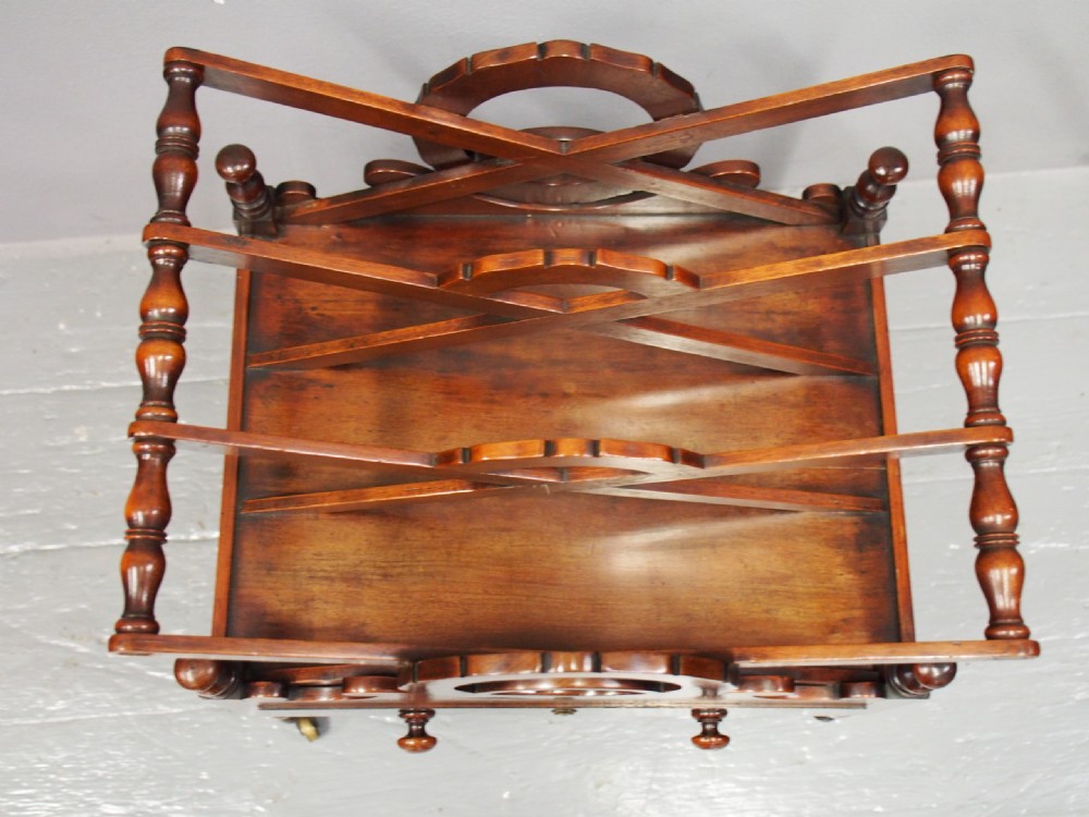 A George IV mahogany Canterbury featuring carved circular dividers, turned corner posts, a single base drawer with two wooden turned knobs, and legs set on brass castors. View VI