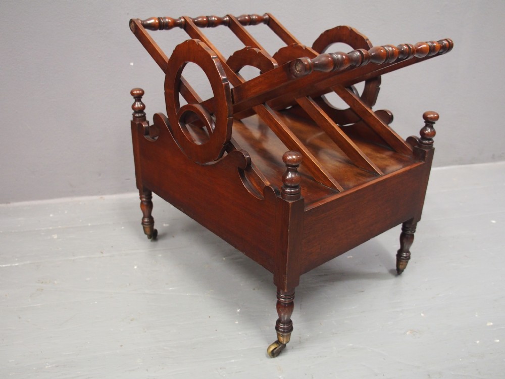 A George IV mahogany Canterbury featuring carved circular dividers, turned corner posts, a single base drawer with two wooden turned knobs, and legs set on brass castors. View VII