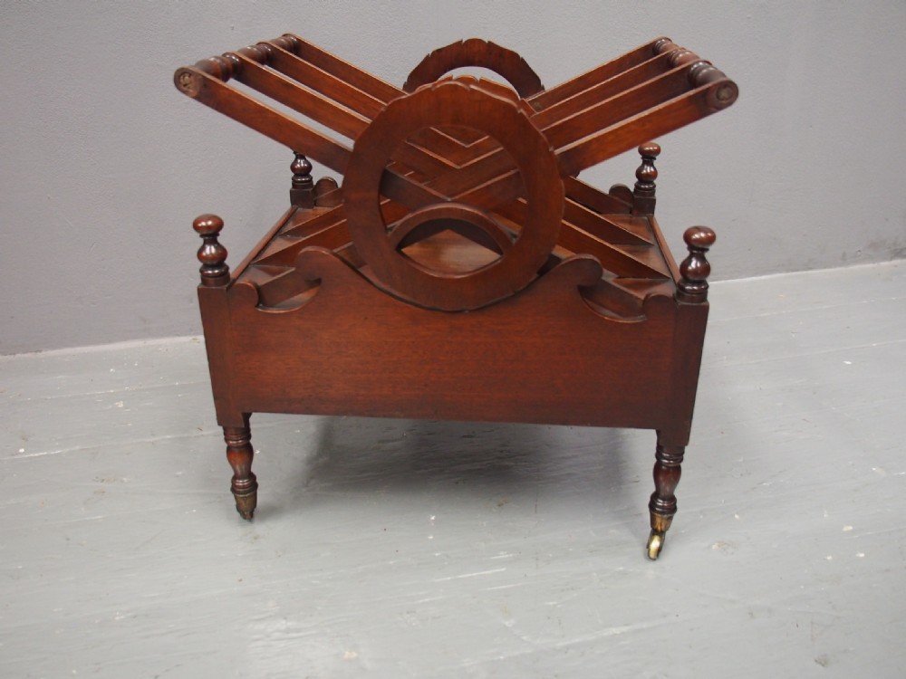 A George IV mahogany Canterbury featuring carved circular dividers, turned corner posts, a single base drawer with two wooden turned knobs, and legs set on brass castors. View VIII