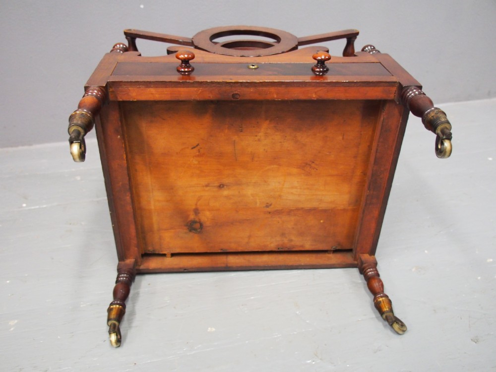 A George IV mahogany Canterbury featuring carved circular dividers, turned corner posts, a single base drawer with two wooden turned knobs, and legs set on brass castors. View IX