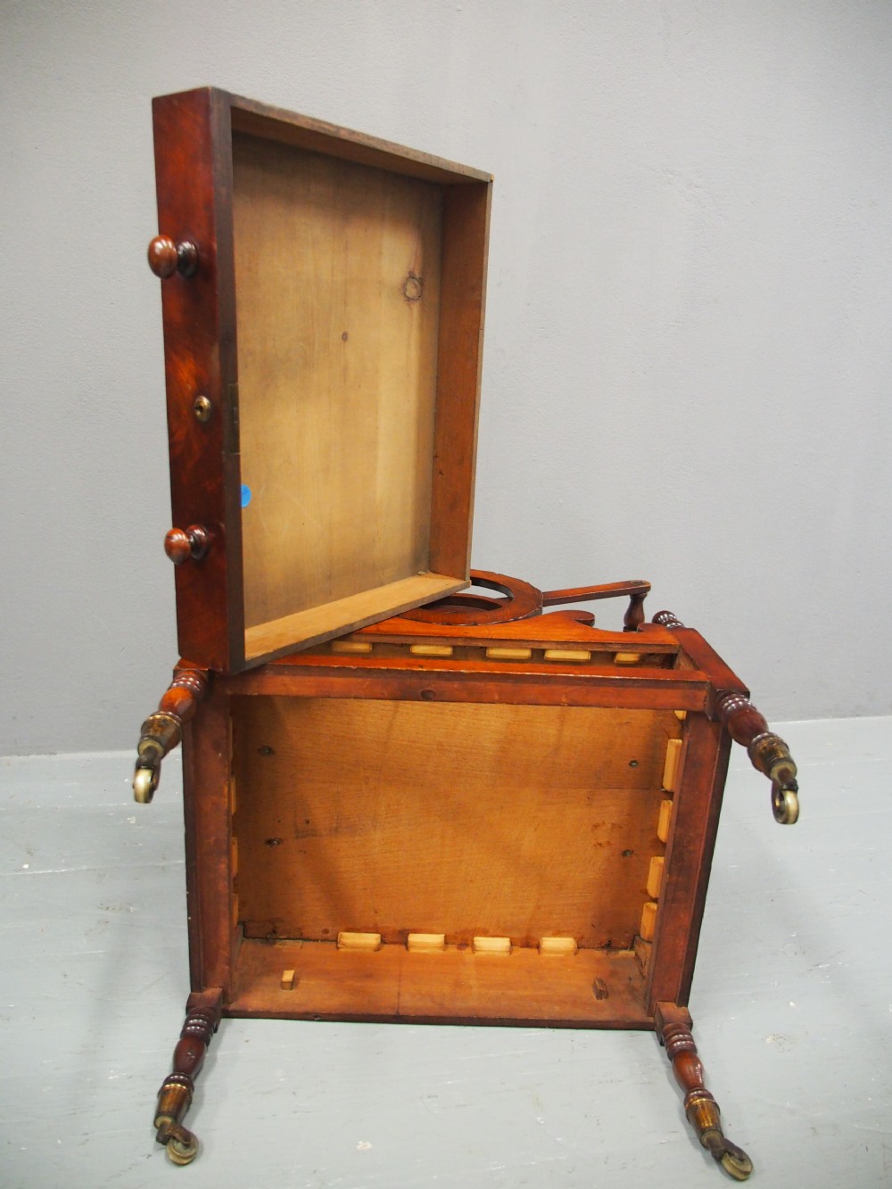 A George IV mahogany Canterbury featuring carved circular dividers, turned corner posts, a single base drawer with two wooden turned knobs, and legs set on brass castors. View X