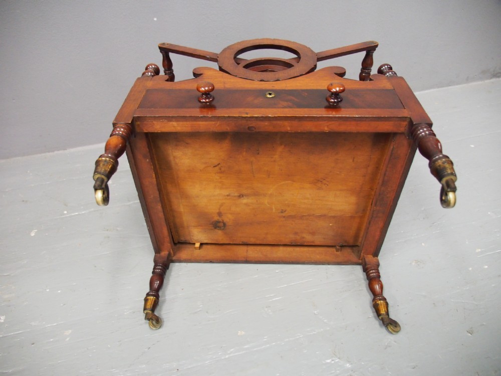 A George IV mahogany Canterbury featuring carved circular dividers, turned corner posts, a single base drawer with two wooden turned knobs, and legs set on brass castors. View XII