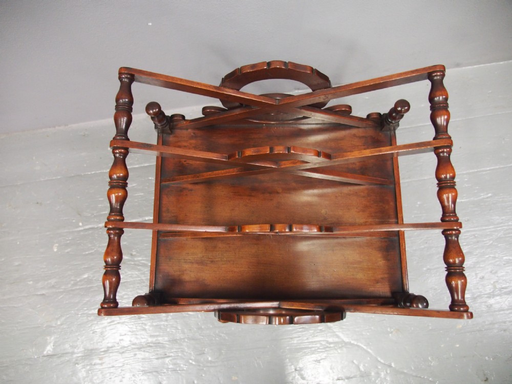 A George IV mahogany Canterbury featuring carved circular dividers, turned corner posts, a single base drawer with two wooden turned knobs, and legs set on brass castors. View XIII