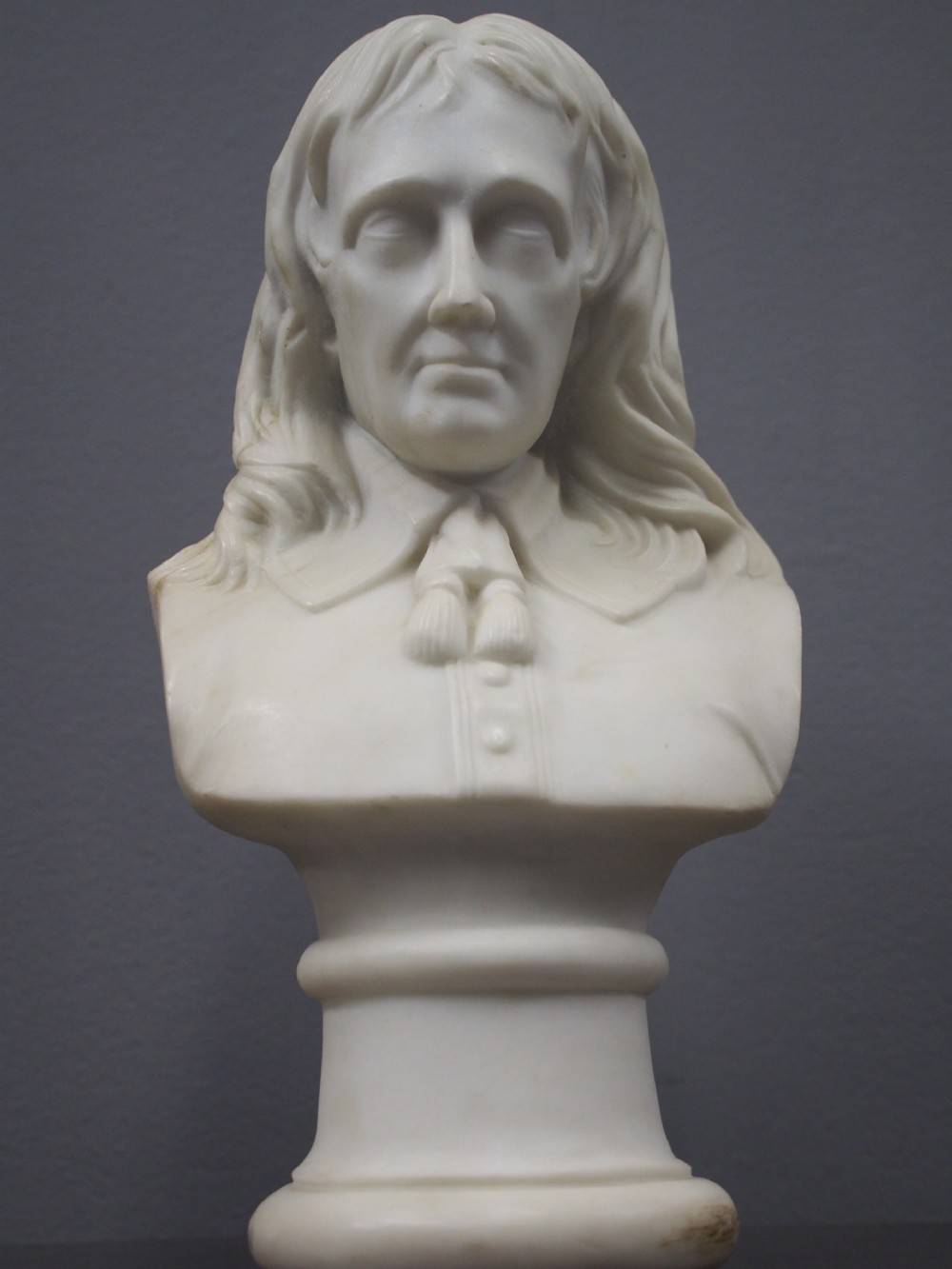 A white marble carved portrait bust depicting a gentleman with long flowing hair and period attire mounted on a round socle base. View II