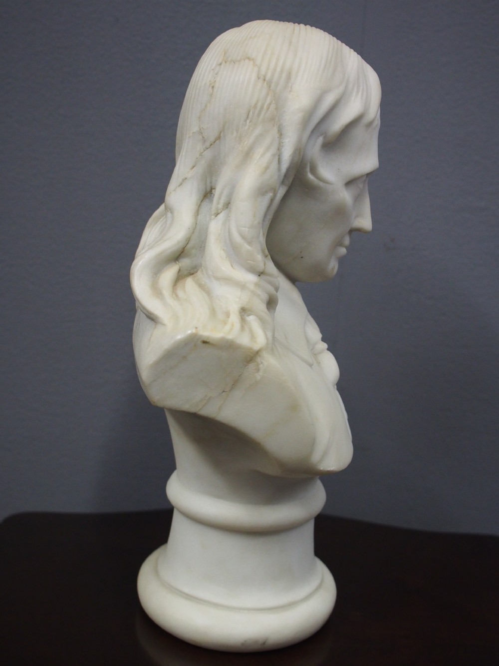 A white marble carved portrait bust depicting a gentleman with long flowing hair and period attire mounted on a round socle base. View IV