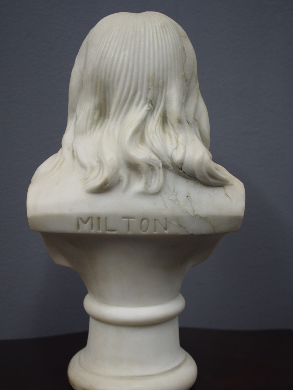 A white marble carved portrait bust depicting a gentleman with long flowing hair and period attire mounted on a round socle base. View V