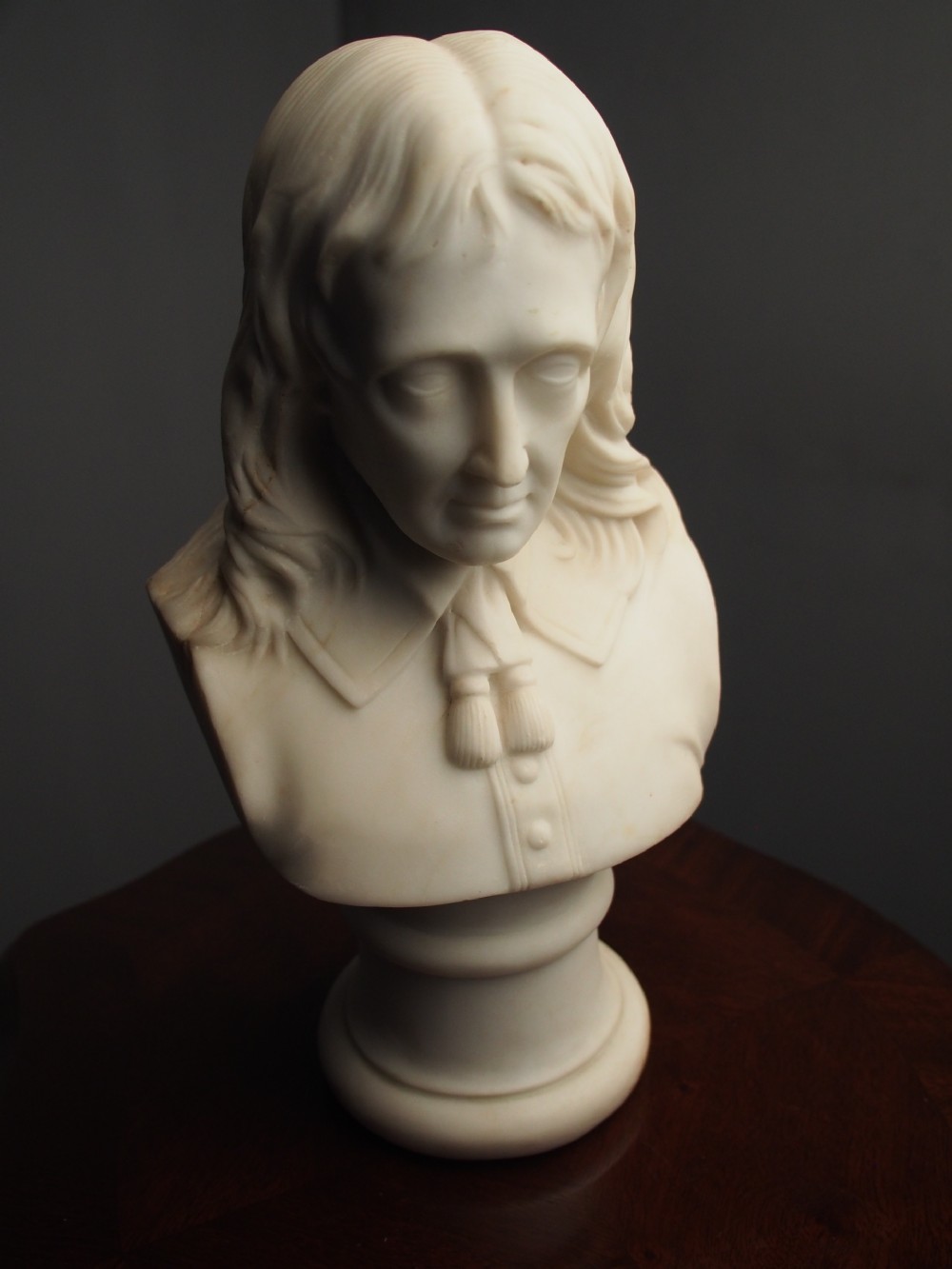 A white marble carved portrait bust depicting a gentleman with long flowing hair and period attire mounted on a round socle base. View IX