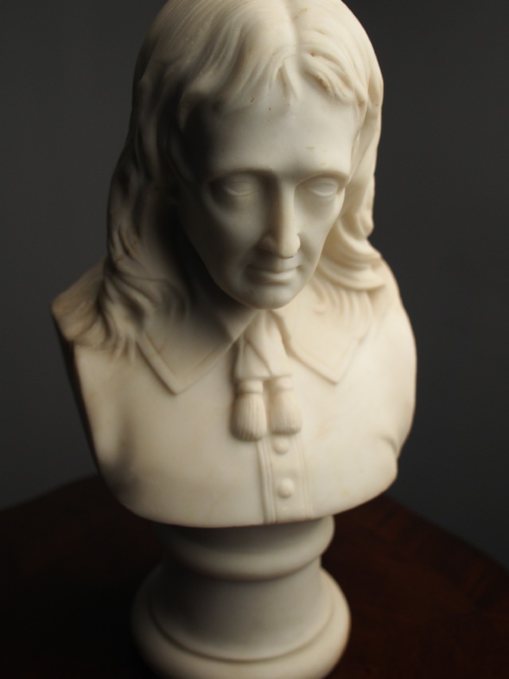 A white marble carved portrait bust depicting a gentleman with long flowing hair and period attire mounted on a round socle base. View X
