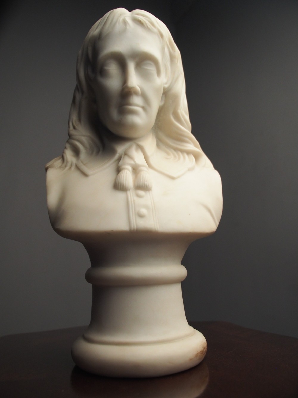 A white marble carved portrait bust depicting a gentleman with long flowing hair and period attire mounted on a round socle base. View XI