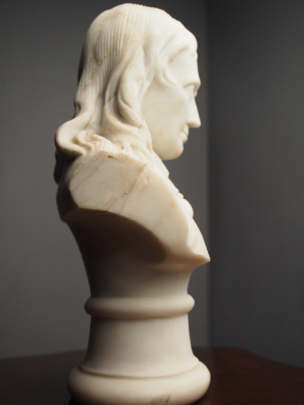 A white marble carved portrait bust depicting a gentleman with long flowing hair and period attire mounted on a round socle base. View XII
