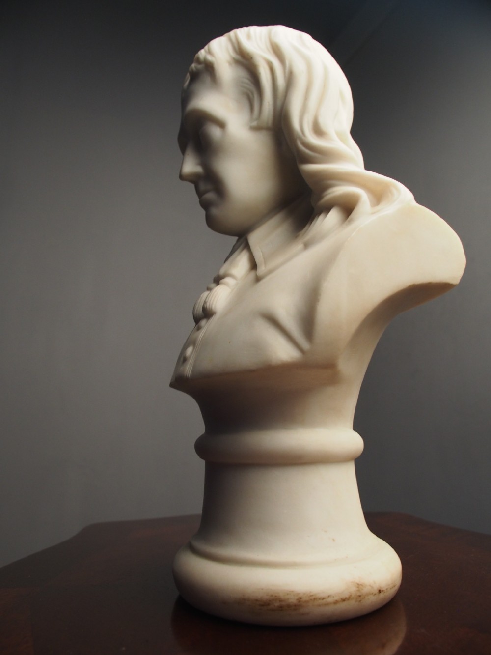 A white marble carved portrait bust depicting a gentleman with long flowing hair and period attire mounted on a round socle base. View XIV