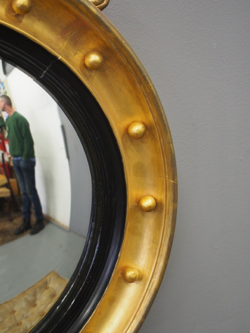A circular gold giltwood convex mirror featuring a carved acanthus leaf crest, ebonised inner slip, and spherule studs around the frame. View V