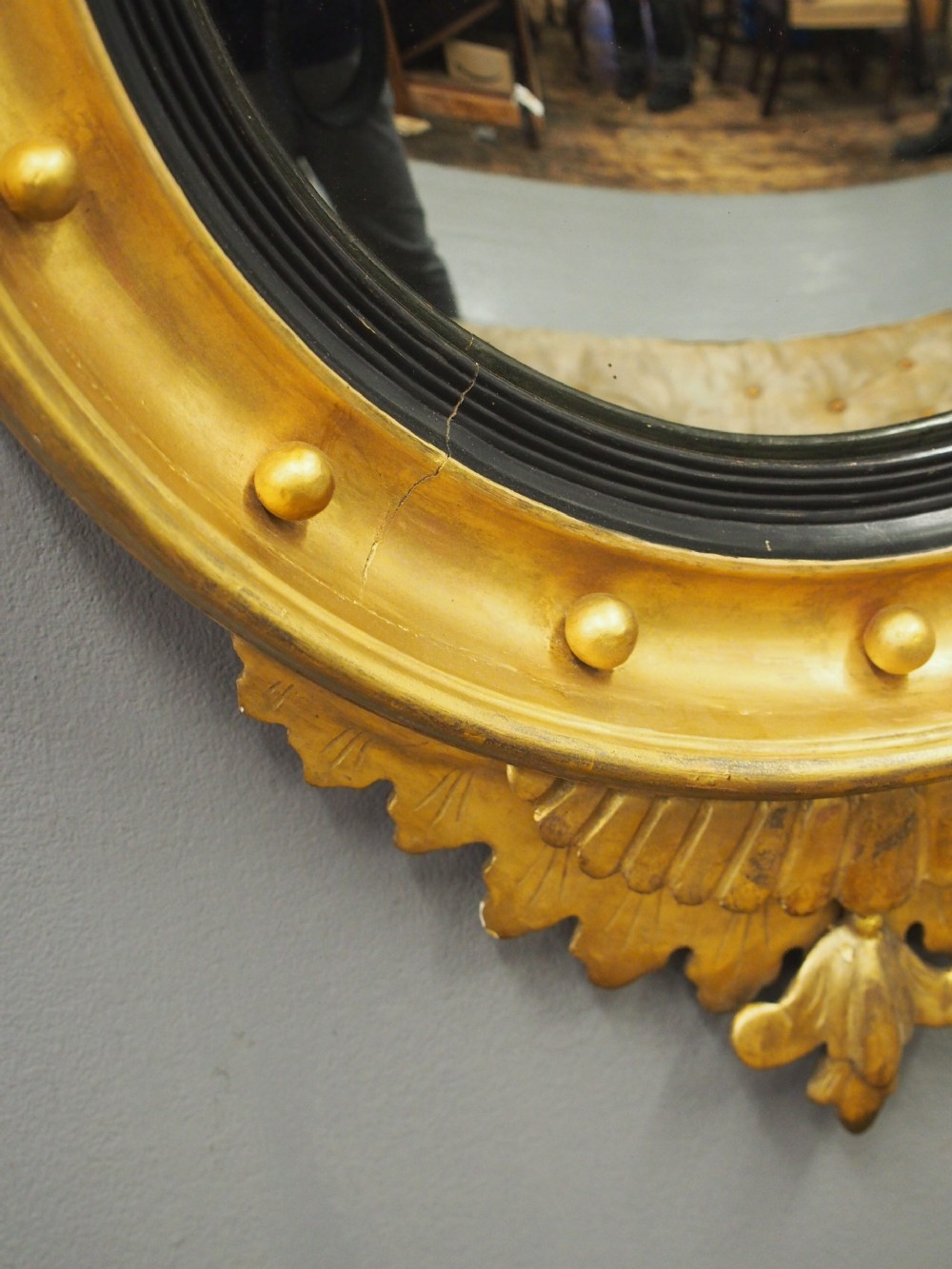 A circular gold giltwood convex mirror featuring a carved acanthus leaf crest, ebonised inner slip, and spherule studs around the frame. View VII