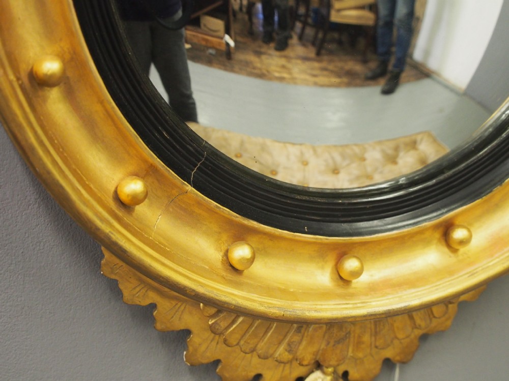A circular gold giltwood convex mirror featuring a carved acanthus leaf crest, ebonised inner slip, and spherule studs around the frame. View VIII