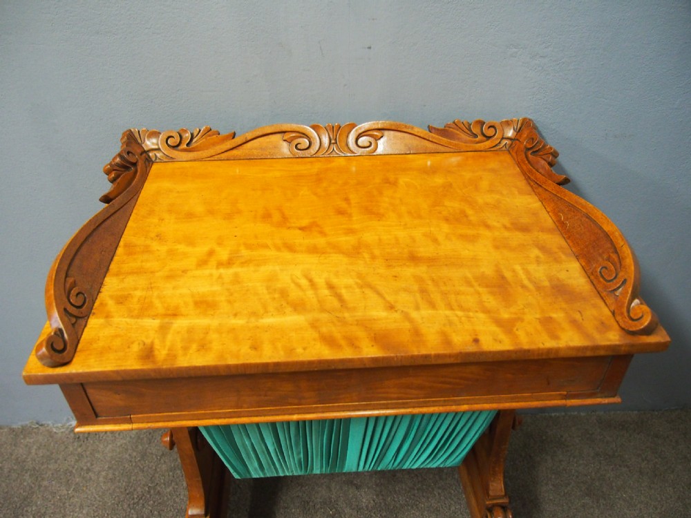 A Victorian satinwood work table featuring a carved top gallery, single drawer, pleated green silk work well, and carved trestle legs. View VII