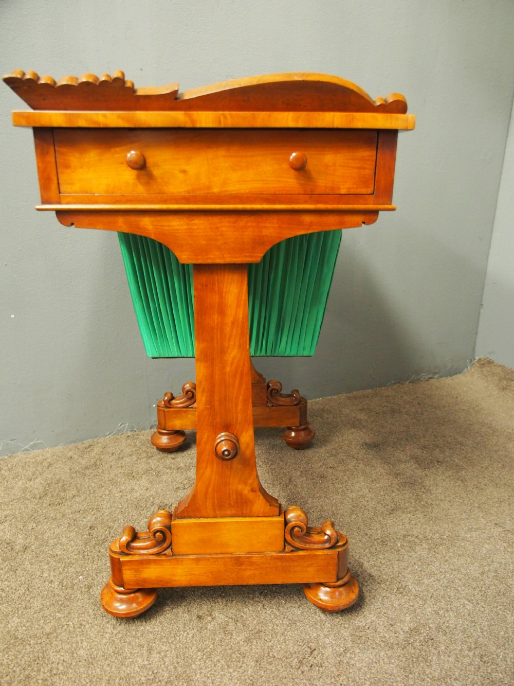 A Victorian satinwood work table featuring a carved top gallery, single drawer, pleated green silk work well, and carved trestle legs. View VIII