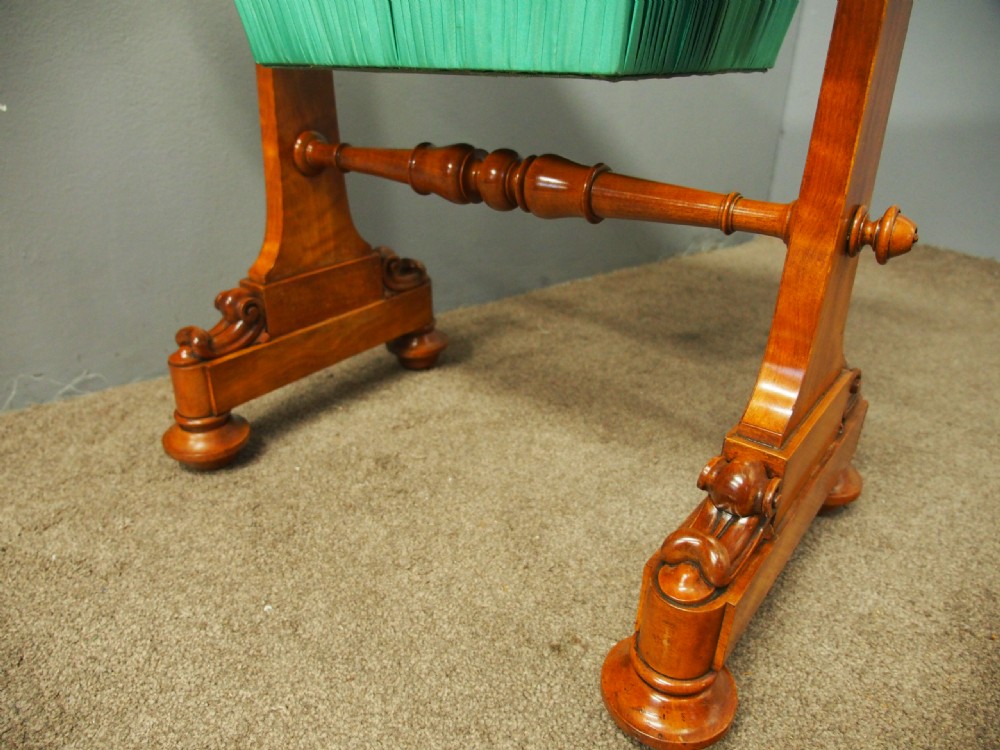 A Victorian satinwood work table featuring a carved top gallery, single drawer, pleated green silk work well, and carved trestle legs. View X