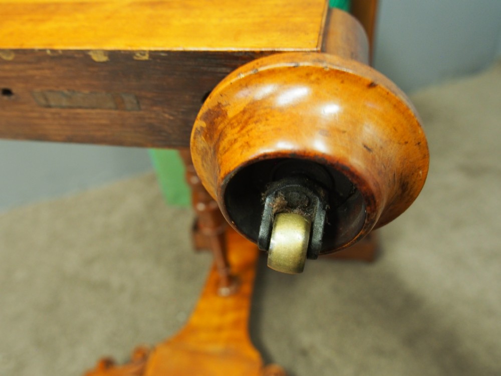 A Victorian satinwood work table featuring a carved top gallery, single drawer, pleated green silk work well, and carved trestle legs. View XI