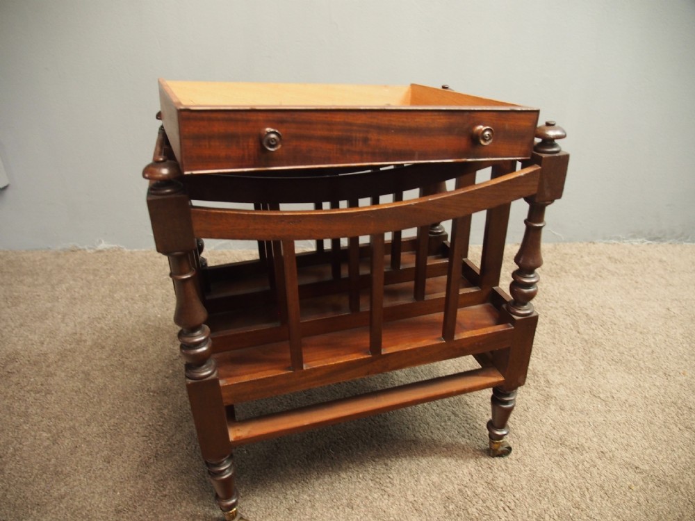 A George IV mahogany three-division Canterbury featuring turned corner posts with finials, slatted partitions, a single base drawer, and turned legs on brass castors. View VI