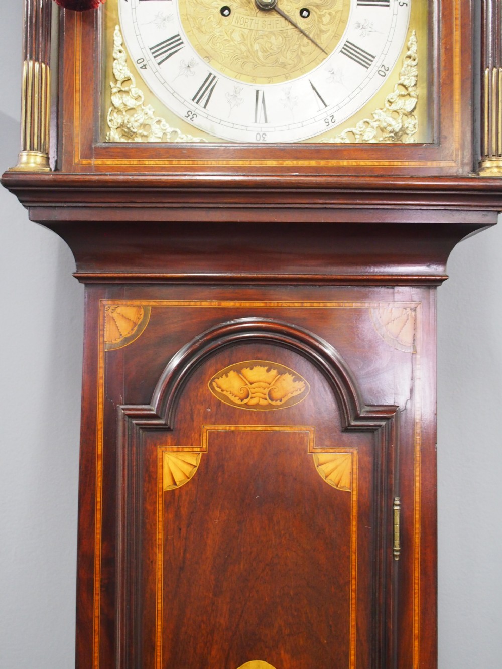 A tall Victorian mahogany longcase clock featuring a swan-neck pediment with fretwork, marquetry inlay, and a brass dial face. View V