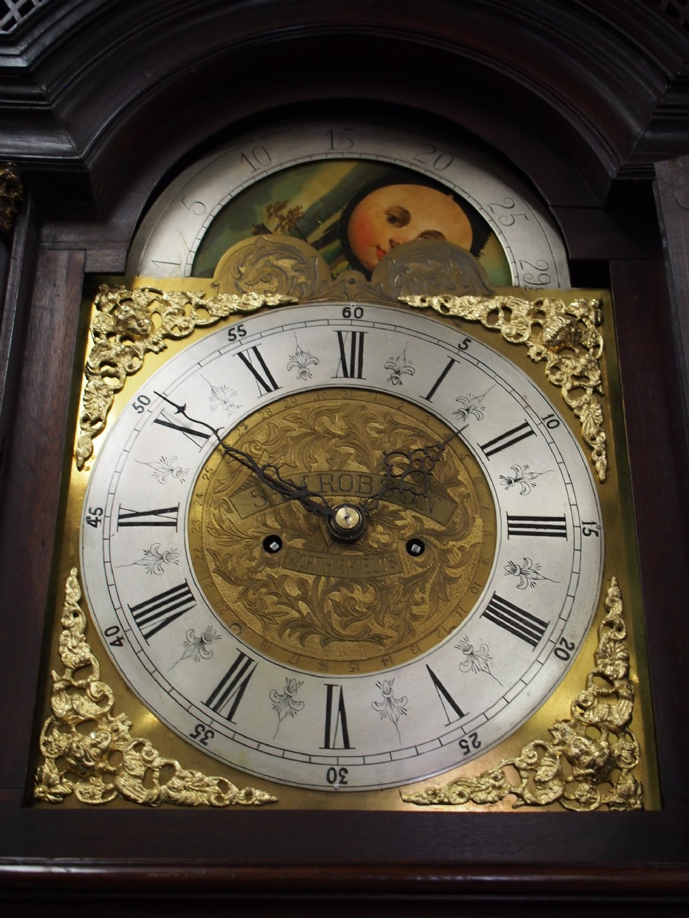 A tall Victorian mahogany longcase clock featuring a swan-neck pediment with fretwork, marquetry inlay, and a brass dial face. View XII