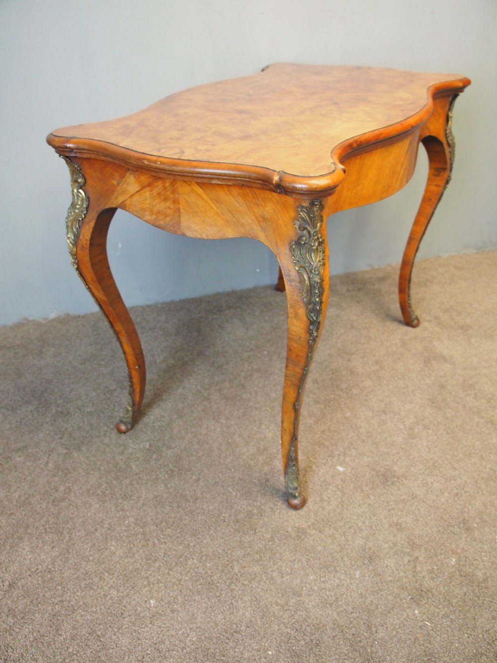 A Louis XV style burr walnut bureau plat featuring a serpentine top, cabriole legs, and ornate gilt-bronze mounts. View II