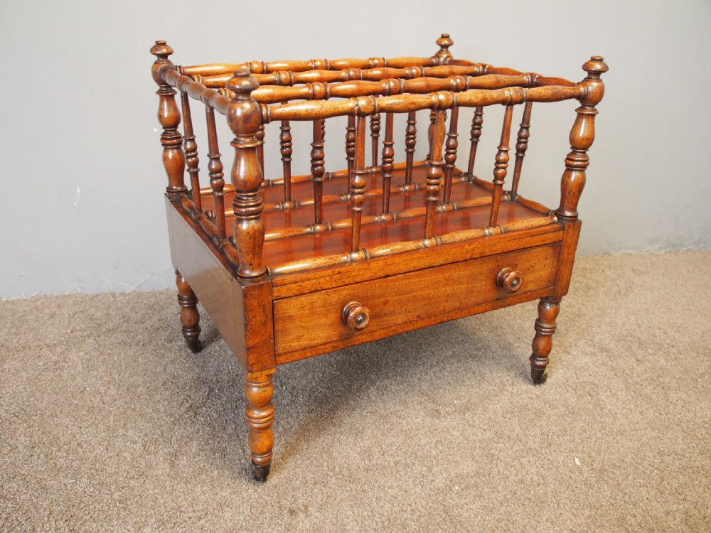 A George IV mahogany Canterbury featuring four slatted compartments with turned spindles, a single base drawer with turned wooden knobs, and turned legs ending in brass castors. View II