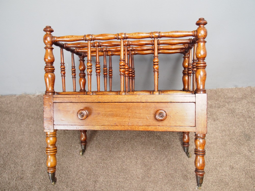 A George IV mahogany Canterbury featuring four slatted compartments with turned spindles, a single base drawer with turned wooden knobs, and turned legs ending in brass castors. View IV
