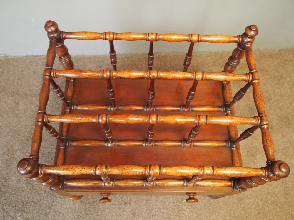 A George IV mahogany Canterbury featuring four slatted compartments with turned spindles, a single base drawer with turned wooden knobs, and turned legs ending in brass castors. View V