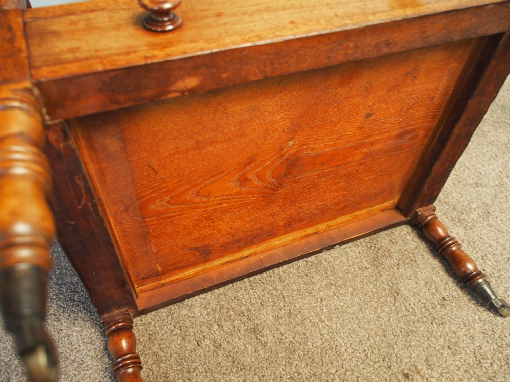 A George IV mahogany Canterbury featuring four slatted compartments with turned spindles, a single base drawer with turned wooden knobs, and turned legs ending in brass castors. View X