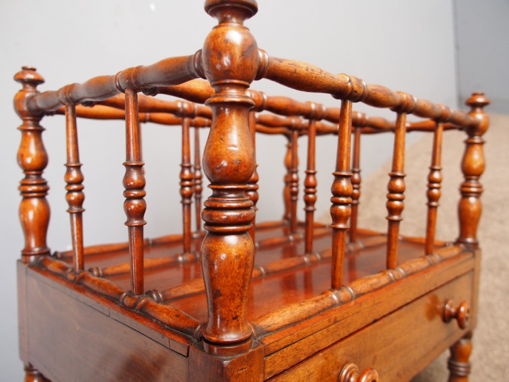 A George IV mahogany Canterbury featuring four slatted compartments with turned spindles, a single base drawer with turned wooden knobs, and turned legs ending in brass castors. View XI