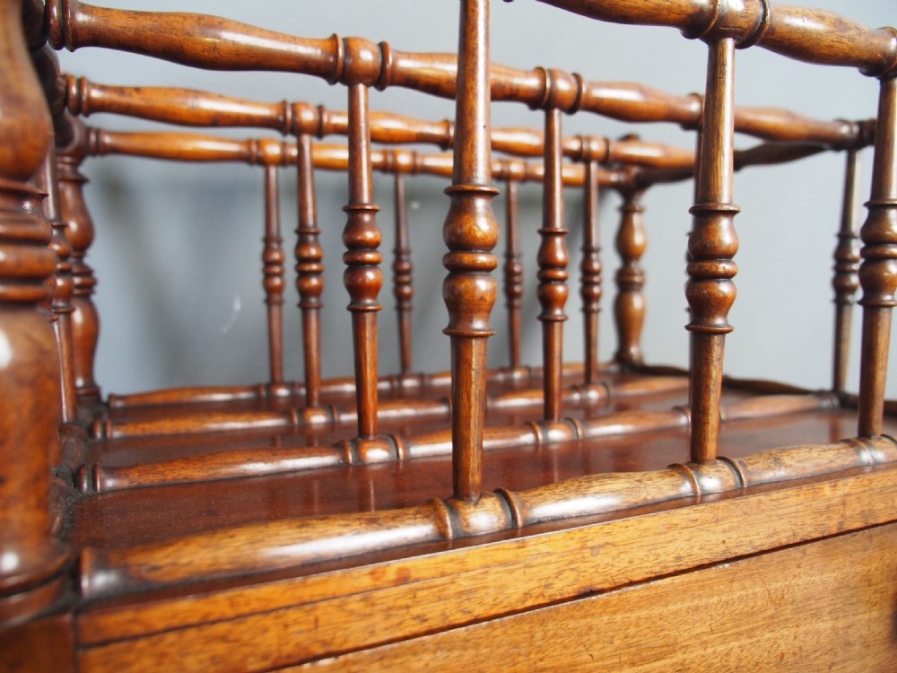 A George IV mahogany Canterbury featuring four slatted compartments with turned spindles, a single base drawer with turned wooden knobs, and turned legs ending in brass castors. View XII