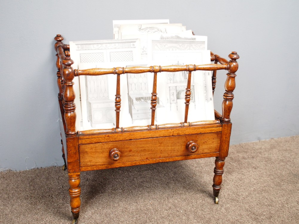 A George IV mahogany Canterbury featuring four slatted compartments with turned spindles, a single base drawer with turned wooden knobs, and turned legs ending in brass castors. View XV