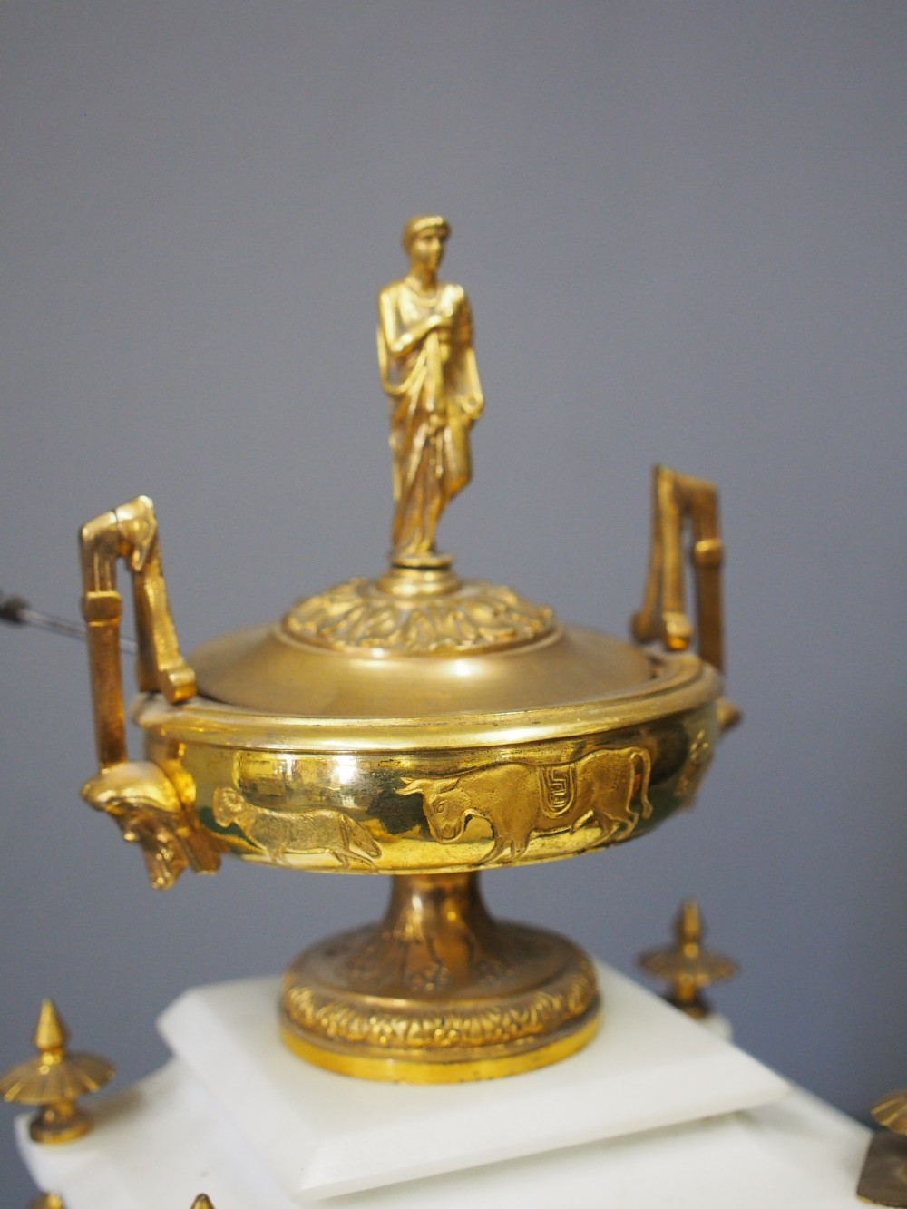 A white marble mantel clock featuring gilt bronze mounts, winged griffin corner supports, and a classical urn finial topped with a standing figure. View III